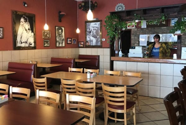Empty tables of Margarita's Family restaurant with a woman behind the counter.
