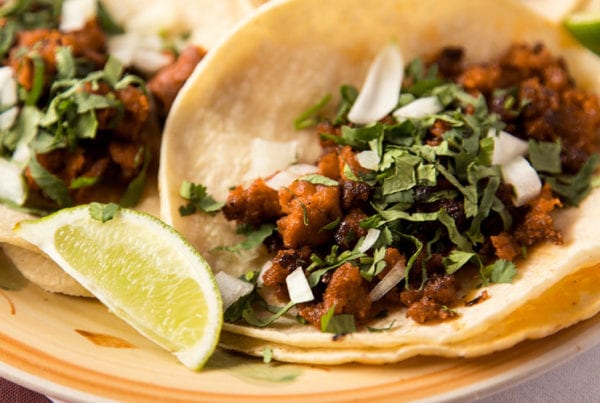 A close-up of a carnitas street taco with cilantro, chopped onion and lime.